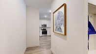 This single-floor, 2-bedroom, 2-bathroom residence is designed with a clean, modern aesthetic and a practical layout that maximizes comfort and functionality. Light wood-style flooring flows through the main living areas, complemented by neutral walls and contemporary finishes throughout.

The kitchen is a standout feature, boasting white shaker cabinetry, a white quartz countertop, classic subway tile backsplash, and a full suite of stainless steel appliances including a range, microwave, and dishwasher. A peninsula island with seating for two, illuminated by pendant lighting, connects the kitchen to the living area, making it ideal for entertaining.

The living room is bright and welcoming, featuring a large window that invites natural light and outdoor views. A hallway with recessed lighting leads through the unit, keeping the flow between spaces seamless.

The primary bedroom is generously sized, featuring plush carpet, a ceiling fan, and access to both a walk-in closet and a private en-suite bathroom. The en-suite offers a double-sink vanity with white cabinetry, quartz countertops, and a glass-enclosed walk-in shower. The second bedroom is equally comfortable, with carpet flooring, a ceiling fan, and a bright window. The second bathroom includes a soaking tub with shower combination and a single-sink vanity. Two dedicated closets provide ample storage throughout the home.