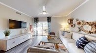 This thoughtfully designed single-floor residence offers a seamless blend of comfort and modern style. The open-concept living and dining area is anchored by wood-look flooring, crown molding, and a ceiling fan, creating a bright and welcoming atmosphere. Large sliding glass doors flood the living room with natural light and open directly onto a private balcony, perfect for outdoor relaxation. Decorative curtains and tasteful wall accents add a warm, curated feel to the space.

The dining area is defined by its clean lines and crown molding detail, comfortably accommodating a round table and chairs with room to spare. Adjacent to the living space, the kitchen is outfitted with white shaker-style cabinetry, quartz countertops, a subtle tile backsplash, stainless steel appliances including a range with overhead hood, built-in microwave, and dishwasher — a functional and attractive space for everyday cooking.

Both bedrooms feature plush carpet flooring and generous natural light from multiple windows with blinds. The primary bedroom includes access to a walk-in closet. Each bathroom is finished with white cabinetry, quartz countertops, and brushed nickel fixtures, maintaining a clean and contemporary aesthetic consistent throughout the home.