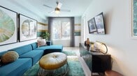 This single-floor residence offers a thoughtfully designed layout that seamlessly connects key living areas. The kitchen is a standout feature, outfitted with taupe flat-front cabinetry, stainless steel appliances including a gas range, microwave, dishwasher, and refrigerator, complemented by a classic white subway tile backsplash and light hardwood-style flooring. Track lighting and an adjacent dining bar with seating enhance both functionality and style.

The open living area flows naturally from the kitchen and is characterized by bold horizontal stripe wall accents in gold and teal, light hardwood flooring, a ceiling fan, and a large window that brings in natural light and views of lush outdoor greenery.

The bedroom provides a comfortable retreat, featuring plush carpeting, a ceiling fan, a dramatic geometric-patterned accent wall in deep navy, and a window with outdoor views.

The bathroom is well-appointed with a floating taupe vanity, white quartz countertop, a large mirror with overhead lighting, and open shelving for storage.

A private balcony extends the living space outdoors, featuring sleek dark tile cladding, a contemporary metal railing, and views of a pool and palm trees below — ideal for relaxing or entertaining.