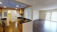 Located at 799 W Fifth Ave in Naperville, IL, this single-floor residence offers a well-organized layout designed for comfortable everyday living. The kitchen is a functional galley-style space featuring warm wood cabinetry, dark granite countertops with a mosaic tile backsplash, stainless steel appliances including a refrigerator and range, and a drop-panel ceiling with recessed lighting. A pass-through opening connects the kitchen to the main living area, enhancing the open feel between spaces. The living room is generously sized, featuring rich dark hardwood-style flooring, a textured ceiling, a ceiling fan, and a baseboard heating system. A sliding glass door floods the space with natural light and provides direct access to an outdoor balcony with views of surrounding greenery. The bedrooms are carpeted and offer a cozy, quiet atmosphere, each equipped with a ceiling fan and vertical blinds over windows that overlook outdoor greenery. Closet space is provided within the bedrooms, including a walk-in style closet with a rod and open shelving. The bathroom is clean and straightforward, featuring a full soaking tub with an overhead shower, white square tile surround, and chrome fixtures. Throughout the unit, warm beige walls and consistent finishes create a cohesive and inviting ambiance.