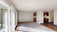 This single-floor, 2-bedroom, 1-bathroom residence offers a practical and comfortable layout designed to maximize everyday livability. The combined living and dining area serves as the heart of the home, featuring neutral-toned carpet, a textured ceiling, and large sliding glass doors that flood the space with natural light while providing direct access to an outdoor green area. The open sightline into the kitchen creates a connected, airy feel throughout the common areas.

The kitchen is outfitted with rich, warm-toned wood cabinetry, light stone-finish countertops, a stainless steel sink, and a white electric range — all set atop hardwood-style flooring that adds a polished contrast to the cabinetry.

Both bedrooms are carpeted and offer a quiet, neutral atmosphere. Each room includes a built-in closet, and the primary bedroom provides a comfortable, well-proportioned retreat. In total, the home features four closets, offering generous storage throughout. A connecting hallway links the bedrooms to the full bathroom, which includes a tiled tub-and-shower combination, hardwood-style flooring, a wood vanity with a stone-finish countertop, and clean white fixtures.

The textured walls and ceilings appear consistently throughout, giving the home a cohesive character. Wall-mounted heating units are present in the bedrooms, and the outdoor surroundings feature lush greenery visible from multiple rooms.