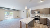 This 2-bedroom, 2-bathroom unit is thoughtfully designed across a single floor, offering a functional and modern living experience. The open-concept kitchen and living area serves as the heart of the home, featuring wood-look plank flooring, rich dark cabinetry, a mosaic tile backsplash, and a full suite of stainless steel appliances including a refrigerator, range, microwave, and dishwasher. A freestanding island with a marble-style countertop and built-in shelving provides additional prep and storage space, illuminated by stylish pendant lighting overhead. The living area extends naturally from the kitchen, finished with plush carpeting and sliding glass doors that lead to a private balcony with outdoor views. The spacious primary bedroom features carpet flooring, a generous footprint, large windows that invite natural light, and access to a dedicated closet. The second bedroom is similarly carpeted and bright. Both bathrooms are finished with wood-look tile flooring, dark wood vanities with white countertops, and large mirrors. The primary bath includes a walk-in shower with a glass enclosure, while the second bath offers a clean, well-lit layout. A hallway connects all rooms efficiently, with two closets providing ample storage throughout the unit.