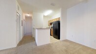 Located at 1234–1244 Floral Springs Blvd in Port Orange, Florida, this single-story residence offers a functional and comfortable layout designed for everyday living. The open-concept living area is generously proportioned, featuring neutral-toned carpeting, high ceilings, and a ceiling fan that contribute to a bright and airy atmosphere. Large windows and a glass-panel door flood the space with natural light and provide outdoor views of the surrounding Florida landscape, including glimpses of mature palm trees.

The kitchen is efficiently designed with warm-toned wood cabinetry, black appliances including a refrigerator and range, and light tile flooring. A peninsula counter serves as a natural divider between the kitchen and the living area, offering additional prep space and casual seating potential.

The bedrooms are well-sized, carpeted, and finished with clean white walls. At least one bedroom includes a ceiling fan and a window with blinds for light control, while another features a closet with bifold doors, providing practical storage. A hallway connects the rooms, maintaining an organized flow throughout the unit.

The bathroom is equipped with a wide vanity countertop, white cabinetry, dual mirrors, and a single basin sink, offering ample counter space and storage. The overall design is clean, neutral, and move-in ready.