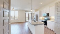 This well-appointed one-bedroom, one-bathroom unit offers a thoughtfully designed open-concept layout across a single floor. Wood-look flooring flows consistently throughout the space, lending warmth and visual continuity to every room.

The combined kitchen and living area serves as the heart of the unit. The kitchen is outfitted with white shaker cabinetry, granite countertops, a subway tile backsplash, and a full suite of stainless steel appliances, including a side-by-side refrigerator, electric range, built-in microwave, and dishwasher. A central island with an undermount sink and pendant lighting above provides additional prep space and casual seating. A built-in desk with open shelving adds a functional workspace. French doors lead to a private balcony, filling the living area with natural light and offering outdoor views. A ceiling fan overhead adds to the comfort of the space.

The bedroom is a well-sized, naturally lit room with a ceiling fan and a large window framing outdoor views. It connects to a walk-in closet with multi-tier shelving. The bathroom features a granite-topped vanity with gray cabinetry, subway-tiled tub-shower combination, and tile flooring. An in-unit laundry area completes this efficiently designed home.