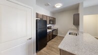 This single-story residence in San Marcos, Texas offers a well-designed 2-bedroom, 2-bathroom layout with a consistent, modern aesthetic throughout. Wood-look plank flooring extends across the main living areas and bedrooms, providing a cohesive look, while neutral gray and beige tones on the walls create a clean, versatile backdrop.

The kitchen is a functional centerpiece, featuring dark espresso cabinetry, granite-look countertops, and black appliances including a full-size refrigerator, range, microwave, and dishwasher. A peninsula with an integrated sink and additional counter space extends into the open living area, making it well-suited for both meal prep and casual dining. Ceiling fans are installed in the living area and bedrooms for added comfort.

Each bedroom offers a walk-in or reach-in closet with built-in shelving, and natural light enters through blinds-equipped windows. Both bathrooms maintain a consistent design with dark vanity cabinetry, granite-look countertops, large mirrors, and light tile flooring. One bathroom includes an adjacent walk-in closet with open shelving. An entry door with a sidelight panel allows additional natural light into the unit.