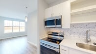 Located at 44–54 Hospital Rd in East Providence, Rhode Island, this single-floor unit offers a thoughtfully designed layout with modern finishes throughout. The kitchen is a standout feature, showcasing crisp white shaker cabinetry, quartz countertops, and a striking marble-patterned tile backsplash. Stainless steel appliances — including an electric range, over-the-range microwave, dishwasher, and refrigerator — complete the space, which flows seamlessly into the living area via light-toned luxury vinyl plank flooring. A pendant light adds a refined touch above the transition space. The bedroom is finished with plush wall-to-wall carpet, generous natural light from a large multi-pane window with outdoor views, and direct access to a closet with built-in shelving. The bathroom features wood-look tile flooring, a full tub-shower combination with brushed nickel fixtures, and a sleek vanity with quartz countertop and warm wood cabinetry. Conveniently, an in-unit stacked washer and dryer is tucked into a dedicated laundry area adjacent to the kitchen. A glass-paneled exterior door provides additional natural light and outdoor access, rounding out this well-appointed, low-maintenance living space.