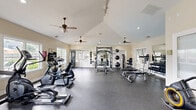 Located at 140 N Davis Rd in LaGrange, Georgia, this dedicated fitness center offers a generously sized, single-floor exercise room designed to support a comprehensive workout experience. The space is characterized by soaring vaulted ceilings that lend an open, airy atmosphere, while multiple ceiling fans are strategically positioned throughout to ensure comfortable air circulation during workouts.

Natural light floods the interior through numerous windows positioned along the walls, offering views of the surrounding outdoor greenery. The durable, dark rubber flooring provides both safety and functionality across the entire workout area.

The facility is comprehensively equipped for both cardio and strength training. Cardio equipment includes multiple treadmills, elliptical machines, stationary bikes, and a rowing machine, all arranged to maximize open floor space. The strength training section features a cable and multi-use power rack, a full dumbbell rack with a broad range of weights, adjustable benches, a weight machine, and a medicine ball station. Wall-mounted mirrors enhance the sense of space and allow for proper form checks during exercise.

Recessed lighting and track lighting supplement the natural light, ensuring the space remains bright throughout the day. The clean, neutral-toned walls and well-organized layout create a focused, professional environment well-suited for a wide range of fitness activities.