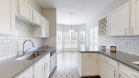 This well-appointed single-story home offers three bedrooms and two bathrooms across a generously sized floor plan. The living room serves as a central highlight, featuring soaring ceilings, transom windows that draw in natural light, a ceiling fan, dark hardwood-style flooring, and a classic fireplace — creating an inviting and airy atmosphere. The entryway welcomes guests with large windows fitted with white wood blinds and additional transom windows above the front door.

The kitchen is designed for both function and style, showcasing white shaker cabinetry, grey quartz countertops, a white subway tile backsplash, stainless steel appliances, and a built-in wine rack. A bright breakfast nook with a bay window and pendant light provides a charming dining area adjacent to the kitchen.

The primary bedroom offers plush carpeting, neutral grey walls, a walk-in closet, and direct access to an en suite bathroom equipped with both a separate glass-enclosed shower and a soaking tub. The secondary bathroom mirrors this clean aesthetic with a tub-shower combo and white vanity cabinetry. Additional bedrooms feature soft carpet flooring, ample natural light from windows with transom detailing, and generous closet space — making this home both comfortable and practical.