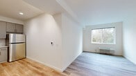 This well-appointed 2-bedroom, 1-bathroom residence offers a clean, modern aesthetic across a single level, thoughtfully designed to maximize functionality. Light wood-style flooring flows consistently throughout the space, complementing the bright white walls that create a fresh, airy atmosphere.

The kitchen is efficiently designed and features gray shaker-style cabinetry, white subway tile backsplash, light countertops, and a full suite of stainless steel appliances including a refrigerator, electric range, and over-the-range microwave. The adjacent living area benefits from natural light and an open connection to the rest of the unit.

The primary bedroom is a comfortable and well-proportioned room with a large window framing serene views of mature trees and greenery. A wall-mounted HVAC unit provides individual climate control. The second bedroom also features a window with wooded views and continues the same light flooring and neutral color palette.

The full bathroom is finished in clean white tones, offering a tub/shower combination with a curtain rod, a vanity with mirror, and wood-style flooring. A notable convenience is the in-unit stacked washer and dryer, tucked neatly alongside a built-in shelving closet, accessible from the hallway. The overall ambiance is bright, clean, and move-in ready.