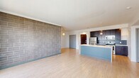 Located at 501 Virginia Ave in Indianapolis, this well-appointed 2-bedroom, 2-bathroom residence offers a thoughtfully designed open-concept layout with modern finishes throughout. The combined living and kitchen area serves as the heart of the home, anchored by a striking full-height brick accent wall that adds texture and character. Light hardwood-style flooring flows throughout the main living spaces, while large sliding glass doors lead to a private balcony with open city views, flooding the area with natural light. The kitchen features dark espresso cabinetry, a subway tile backsplash, stainless steel appliances, and a spacious peninsula with a built-in sink — ideal for both meal prep and casual dining. Pendant lighting overhead adds a contemporary touch. Both bedrooms are carpeted for comfort; the primary bedroom offers a generous footprint with a walk-in closet outfitted with built-in shelving and hanging rods. The second bedroom benefits from dual windows that invite additional natural light. Each bathroom is clean and functional, featuring light wood-style flooring, a full soaking tub with shower, and warm wood-toned vanity cabinetry with a white countertop. Two hallways and two closets round out the practical layout of this modern urban residence.