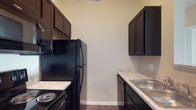 Located at 5927 Avery Wood Ave in Dublin, Ohio, this single-floor residence offers a thoughtfully designed living space in a desirable community. The kitchen is a standout feature, showcasing rich dark espresso cabinetry that extends to the ceiling for generous storage capacity. Light-toned laminate countertops provide a striking contrast against the dark cabinetry, while black appliances — including a refrigerator, range, built-in microwave, and dishwasher — create a cohesive and modern aesthetic. A stainless steel sink is conveniently positioned along the countertop, complementing the functional galley-style layout that maximizes efficiency. The kitchen's neutral walls and wood-look flooring contribute to a warm yet contemporary ambiance. The ceiling height adds an open, airy feel to the space, and the clean, neutral color palette throughout provides a versatile backdrop suited to a variety of interior styles. This residence combines practical design with modern finishes, making it a well-suited home in the Dublin, Ohio area.