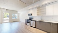 Located at 7288 Maple Street in Mission, BC, this two-bedroom, one-bathroom unit offers a well-designed single-floor layout with a contemporary aesthetic. The open kitchen is a standout feature, outfitted with stainless steel appliances including a refrigerator, electric range, microwave, and dishwasher. Two-toned cabinetry — white uppers with grey lower cabinets — is complemented by a white subway tile backsplash, open shelving, and light countertops. Track lighting runs along the ceiling, adding an industrial-modern touch. Light-toned hardwood-style flooring flows consistently throughout the unit, creating a cohesive and clean look. A window in the living area allows natural light to fill the open space. Both bedrooms are functional and simply designed, with the primary bedroom featuring a sliding-door closet with built-in shelving for efficient storage. A hallway connects the rooms and provides access to the full bathroom, which is finished with a soaker tub and floor-to-ceiling large-format white tiles in a crisp, minimalist style. An in-unit washer and dryer are also visible in the floor plan, adding everyday convenience. The overall ambiance is bright, modern, and efficiently organized.