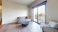 Located at 128 Langdon Street in Madison, Wisconsin, this modern 2-bedroom, 2-bathroom apartment offers 720 square feet of thoughtfully designed single-floor living. The open-concept kitchen and living area serves as the heart of the unit, featuring stainless steel appliances including a Whirlpool refrigerator and range, white quartz countertops with a subway tile backsplash, and gray shaker-style cabinetry. A large kitchen island with seating for three is illuminated by striking dome pendant lights with gold interiors. The living room benefits from abundant natural light through floor-to-ceiling sliding glass doors that open onto a private balcony, offering elevated views of the Madison cityscape and surrounding greenery. Hardwood-style flooring runs throughout the unit. The primary bedroom measures 170 square feet and includes a double-door closet, while both bedrooms feature large windows with roller shades and panoramic urban views. Each of the two bathrooms is finished with white quartz vanity tops, undermount sinks, chrome hardware, and bold circular black-framed mirrors, lending a clean, contemporary aesthetic. The unit's neutral palette and modern finishes create a bright, cohesive atmosphere throughout.