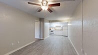 This single-floor unit offers a practical and well-organized layout designed for comfortable everyday living. The open-concept living area flows directly into the kitchen, creating a connected and functional common space. Light gray wood-style flooring runs throughout the living and kitchen areas, lending a clean, cohesive aesthetic, while ceiling fans provide both lighting and ventilation.

The kitchen is efficiently outfitted with white cabinetry extending to the ceiling, granite-look countertops, and white appliances including a range, microwave, and refrigerator. A skylight above the kitchen brings in natural light, brightening the workspace. The sink is centrally positioned beneath the upper cabinets, maximizing counter space on either side.

The bedrooms are carpeted for comfort and each features a ceiling fan. One bedroom includes an attached bathroom, offering added privacy. A window with blinds allows for natural light and ventilation. Closet access is available within the bedroom.

The bathroom is finished in a clean, white palette with a single-sink vanity featuring shaker-style cabinetry, a large mirror with an illuminated fixture above, and a tub/shower combination. Wood-style flooring carries into the bathroom, maintaining a consistent design throughout the unit.