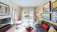 Located at 16 S Division St in Auburn, Washington, this single-floor residence offers a thoughtfully designed open-concept layout with contemporary finishes and a cohesive, vibrant aesthetic. The living area is bright and inviting, anchored by large sliding glass doors dressed with patterned curtains that open to a private outdoor patio. The patio provides a peaceful outdoor retreat with seating space and lush greenery visible beyond.

The kitchen is a functional and stylish centerpiece of the home, featuring dark espresso cabinetry extending to the ceiling for generous storage, stainless steel appliances including a refrigerator, range, and microwave, and a light quartz countertop that wraps around a peninsula with bar seating. Sleek pendant lighting illuminates the counter, making it an ideal casual dining area.

The residence includes two bedrooms, each with plush carpeting, natural light from well-dressed windows, and closet access. The primary bedroom benefits from a walk-in closet, while both rooms offer a calm, restful atmosphere with neutral tones.

Wood-style flooring runs throughout the main living areas, tying together the open layout. The overall ambiance is modern and welcoming, with a balance of bold accent colors and clean architectural lines.