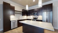 Located at 3600 Park East Drive in Beachwood, OH, this single-floor, 3-bedroom, 2-bathroom residence offers a thoughtfully designed layout with contemporary finishes throughout. The kitchen is a standout feature, showcasing rich dark cabinetry, a classic white subway tile backsplash, light stone countertops, a central island, and a full suite of stainless steel appliances — including a range, microwave, and dishwasher — all illuminated by modern pendant lighting and under-cabinet lights. The living room benefits from large windows with blinds that invite natural light and feature light hardwood-style flooring, creating a bright and welcoming atmosphere. The spacious primary bedroom includes plush carpeting, a ceiling fan, and access to a well-organized walk-in closet with built-in shelving, hanging rods, and a built-in safe. The additional bedrooms offer carpeted or hardwood-style flooring and natural light from large windows. The bathrooms are finished with large-format tile flooring, dark wood vanities, stone countertops, and ample storage cabinetry. Crown molding and neutral tones unify the space, contributing to a clean, modern aesthetic throughout.