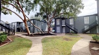 This residential community presents a thoughtfully designed outdoor environment that blends two distinct architectural styles across its grounds. One set of buildings features a contemporary aesthetic with dark gray lap siding, exterior staircases, and clean geometric lines, while another showcases a more traditional design with warm brick facades, bay windows, decorative gabled rooflines, and covered balconies — creating a visually dynamic campus feel.

The grounds are generously landscaped with mature trees providing substantial shade and a natural canopy throughout the property. Curved concrete walkways wind through well-maintained lawns and freshly mulched garden beds, connecting the various buildings in an inviting and accessible layout.

A standout feature of the community is its resort-style pool area, complete with a spacious paver deck, cushioned lounge chairs, and umbrella-shaded table seating — ideal for relaxation and socializing. The pool is bordered by manicured greenery and ornamental plantings that soften the hardscape and add vibrant color.

The overall ambiance of the community is one of comfort and ease, offering a balance of open communal spaces and private residential settings. The combination of mature landscaping, distinct architectural character, and well-appointed outdoor amenities creates an inviting atmosphere throughout the property.