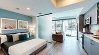 Located at 1509 Broadway in the heart of San Diego, CA, this thoughtfully designed studio offers a smart, efficient single-floor layout that maximizes every square foot. Wide-plank hardwood-style flooring flows throughout, unifying the space with a warm, contemporary aesthetic.

The sleeping area is separated from the living space by a sleek frosted-glass sliding partition, providing privacy without sacrificing the open, airy feel of the unit. A tray ceiling detail above the sleeping area adds architectural depth and visual interest.

The living area is anchored by floor-to-ceiling sliding glass doors that flood the space with natural light and open to direct views of a resort-style pool and courtyard. A ceiling fan complements the light-filled atmosphere. The adjacent kitchen runs along one wall and is well-appointed with stainless steel appliances including a gas range, built-in microwave, and refrigerator, complemented by two-tone cabinetry, a subway tile backsplash, and light stone countertops.

A wide hallway connects the entry to the main living area, with the bathroom situated off to the side. The bathroom features warm tile flooring, a spacious vanity with ample storage, and soothing teal accent walls that carry a cohesive color palette throughout the unit. The overall ambiance is modern, bright, and urbane — ideal for city living in downtown San Diego.