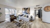 This single-floor residence presents a well-designed open-concept layout that seamlessly connects the living, dining, and kitchen areas. The living room is a generously sized, welcoming space highlighted by wood-look plank flooring, a textured ceiling, and large windows that invite natural light and outdoor views. The room accommodates comfortable seating arrangements and flows naturally toward the kitchen and dining area.

The kitchen is a standout feature, outfitted with bold charcoal cabinetry accented by gold hardware, a classic white subway tile backsplash, butcher block countertops, and a full suite of black appliances including a refrigerator, range, and dishwasher. A bar-height dining table with stools sits adjacent, providing a practical and stylish eat-in space.

The bedrooms offer plush carpeted flooring and ample natural light through generously sized windows with outdoor views. The primary bedroom includes an en-suite vanity area, creating a private and functional retreat. Additional bedrooms maintain the same warm, neutral aesthetic with plenty of space for furnishings.

Throughout the residence, the consistent use of neutral tones, wood-look flooring in main areas, and coordinated finishes create a cohesive and modern ambiance that balances comfort with contemporary style.