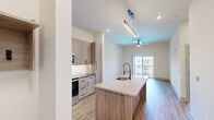 Located at 401 Haysland Rd SW in Huntsville, Alabama, this thoughtfully designed one-bedroom, two-bathroom residence offers a modern living experience with high-quality finishes throughout. The open-concept layout seamlessly connects the kitchen and living area, creating an efficient and inviting space. The kitchen is a standout feature, boasting light wood-tone cabinetry, dark granite countertops, a granite-topped island with an undermount sink and matte black faucet, stainless steel appliances including a refrigerator, electric range, and microwave, plus a tiled backsplash. The living area is finished with wood-look plank flooring, a ceiling fan, and a sliding glass door that opens to a private balcony. The bedroom features plush carpet, a ceiling fan, generous natural light from a large window, and a stylish barn-style sliding door leading to a walk-in closet with wire shelving. The well-appointed bathroom includes a wood-framed mirror, granite vanity, matte black fixtures, and a tiled tub-shower combination. Additional highlights include a dedicated laundry area with a stacked washer and dryer unit, recessed lighting, and clean, neutral tones throughout that create a bright, contemporary ambiance.