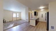This single-floor unit offers a thoughtfully designed open-concept layout that seamlessly connects the living and kitchen areas. The kitchen is a standout feature, equipped with dark espresso cabinetry, stainless steel appliances including a refrigerator, range, and over-the-range microwave, light countertops, and a peninsula with a sink that opens toward the living space. The living area is generously sized, featuring a combination of wood-style hard flooring and plush carpet, creating a warm and comfortable atmosphere. Natural light flows in through windows fitted with horizontal blinds, brightening the cream-toned walls throughout. The bedrooms are carpeted and well-proportioned, each offering sliding or hinged closet storage and baseboard heating units beneath the windows. The unit includes two bathrooms — one full bath with a tub/shower combo, white tile surround, and stone-look tile flooring, and a second half or three-quarter bath featuring a dark vanity with a gray countertop and a large mirror. Warm wood-toned trim and door accents complement the neutral color palette, lending the space a cohesive and clean aesthetic throughout.