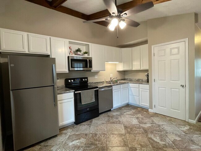Cocina con techo abovedado, ventilador de techo y electrodomésticos que incluyen lavavajillas y microondas de acero inoxidable. - 1277 Tallberry Dr