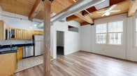 This thoughtfully designed 2-bedroom, 2-bathroom unit at 51 Maple St, Unit 336 in Rockland, MA blends industrial character with modern comfort. The open-concept living and kitchen area serves as the heart of the home, featuring warm hardwood floors, striking exposed wood beam ceilings, and a prominent structural wood post that nods to the building's heritage. An electric fireplace with a classic white mantel anchors the living area, while a bank of large windows fills the space with natural light and views of the surrounding neighborhood. The kitchen is well-appointed with honey-toned wood cabinetry, dark granite countertops, stainless steel appliances including a refrigerator, range, dishwasher, and microwave, and tile flooring. An exposed ductwork detail and pendant lighting add to the loft-like aesthetic. The spacious primary bedroom features the same warm wood beam ceiling, plush carpet, a ceiling fan, and generous natural light. A dedicated walk-in closet with wire shelving provides ample storage. The secondary bedroom offers carpet flooring, a wood beam ceiling, and a unique interior clerestory window. Both bathrooms are finished with tile floors and full tub/shower combinations. The unit's cohesive industrial-meets-residential design creates a distinctive and inviting atmosphere throughout.
