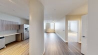 Located in the heart of downtown Rochester, this well-appointed one-bedroom, one-bathroom residence offers a thoughtfully designed single-floor layout with modern finishes throughout. The open-concept kitchen and living area serves as the central hub of the home, featuring wood-grain cabinetry, white quartz countertops, a subway tile backsplash, and a full suite of stainless steel appliances including a double wall oven, dishwasher, and French door refrigerator. Track lighting and warm hardwood-style flooring further elevate the space. A distinctive curved architectural column adds a unique design element to this area. The generously sized bedroom is finished with plush carpeting, track lighting, and large windows that frame sweeping views of the Rochester skyline, filling the room with natural light. The living area also benefits from dual windows offering the same urban vistas. The bathroom is outfitted with large-format tile flooring, a floating wood-toned vanity, a framed mirror, and a glass-enclosed shower. A dedicated in-unit laundry area houses a side-by-side Electrolux washer and dryer, adding everyday convenience. A closet completes the layout, offering practical storage in this polished urban residence.
