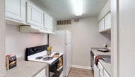 This single-story residence at 4405 N Garland offers a well-organized layout with a cohesive neutral color palette throughout. The living area features wood-look flooring, crown molding, and a textured ceiling, lending a clean and polished feel to the space. A half-wall pass-through connects the living area to the kitchen, while a built-in shelving nook provides a practical decorative touch. Sliding glass doors open to a private patio, and an adjacent window invites natural light into the room.

The galley-style kitchen is outfitted with white cabinetry featuring raised-panel detailing, speckled laminate countertops, and white appliances including a full-size refrigerator, electric range, and dishwasher. A range hood and overhead lighting ensure functionality throughout.

The bedrooms are carpeted and include ceiling fans with light fixtures. The primary bedroom benefits from direct access to a closet and a full bathroom, which features white vanity cabinetry, a framed mirror, speckled countertops, and a well-lit vanity strip above the sink. An additional bedroom offers a window with vertical blinds, providing natural light and a comfortable atmosphere.