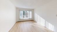 Located at 3630 Renton Ave S in Seattle's Rainier Valley neighborhood, this one-bedroom, one-bathroom unit offers a clean, efficient layout across a single floor. Light wood flooring runs throughout the space, complementing crisp white walls and textured ceilings that lend a classic residential character. The entrance hallway leads naturally into the open-plan kitchen and living area, where white cabinetry provides practical storage and the layout allows for flexible furniture arrangement. Large windows fitted with vertical blinds invite generous natural light into both the living area and the bedroom, creating a bright and airy atmosphere throughout. The bedroom offers a comfortable, well-proportioned space with its own window view and baseboard heating. Four closets distributed throughout the unit ensure ample storage for everyday needs. The bathroom features a full tub-shower combination, a single vanity with under-sink cabinetry, and a wall-mounted mirror, all finished in clean white tones. Baseboard heating is present in multiple rooms, ensuring year-round comfort. The overall aesthetic is simple, neutral, and move-in ready, making this a practical and well-lit home in an accessible Seattle neighborhood.