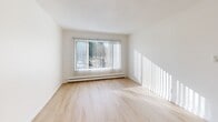 Located at 3630 Renton Ave S in Seattle's Rainier Valley neighborhood, this one-bedroom, one-bathroom unit offers a clean, efficient layout across a single floor. Light wood flooring runs throughout the space, complementing crisp white walls and textured ceilings that lend a classic residential character. The entrance hallway leads naturally into the open-plan kitchen and living area, where white cabinetry provides practical storage and the layout allows for flexible furniture arrangement. Large windows fitted with vertical blinds invite generous natural light into both the living area and the bedroom, creating a bright and airy atmosphere throughout. The bedroom offers a comfortable, well-proportioned space with its own window view and baseboard heating. Four closets distributed throughout the unit ensure ample storage for everyday needs. The bathroom features a full tub-shower combination, a single vanity with under-sink cabinetry, and a wall-mounted mirror, all finished in clean white tones. Baseboard heating is present in multiple rooms, ensuring year-round comfort. The overall aesthetic is simple, neutral, and move-in ready, making this a practical and well-lit home in an accessible Seattle neighborhood.