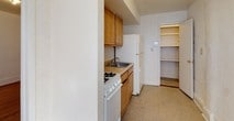 This single-floor residential unit offers a well-defined layout with several distinct living spaces connected by a straightforward floor plan. Throughout the main living and bedroom areas, rich hardwood floors with decorative border inlays are a defining feature, lending warmth and classic character to the space. Large double-hung windows allow generous natural light to fill the rooms, each of which is equipped with a cast-iron radiator for efficient heating. The white walls and tile ceilings maintain a clean, neutral backdrop throughout.

The galley-style kitchen is efficiently arranged with warm wood cabinetry, a gas range, a double sink, and a full-size refrigerator. Durable tile flooring anchors the kitchen, which also connects to a dedicated storage closet with built-in shelving — a practical feature that maximizes organization. 

The bathroom is compact yet complete, outfitted with white subway tile surrounding the bathtub and shower, a pedestal-style vanity with a mirrored medicine cabinet, and tile flooring. Each bedroom offers a quiet, open feel with ample floor space, closet access, and the same consistent hardwood flooring found throughout the unit. Overall, the space presents a functional and classic interior with timeless architectural details.