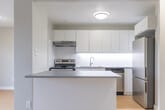 Located at 75 Stewart Street in Oakville, Ontario, this 1-bedroom, 1-bathroom unit offers a thoughtfully designed layout that maximizes its comfortable footprint. The open-concept living and kitchen area serves as the heart of the home, featuring light hardwood-style flooring that flows seamlessly throughout the space. The kitchen is outfitted with crisp white cabinetry extending to the ceiling for ample storage, a grey countertop island that doubles as a breakfast bar, and stainless steel appliances including a dishwasher, electric range, and refrigerator. A double sink and under-cabinet range hood complete the functional setup. The living room is bright and airy, with large sliding glass doors opening onto a private balcony that offers views of the surrounding Oakville neighbourhood. The bedroom is a well-proportioned retreat featuring its own sliding glass door with balcony access, a sliding double-panel closet, a dedicated window for natural light, and baseboard heating. The bathroom is clean and classic, featuring a full soaker tub with tiled surround and chrome fixtures. Neutral grey walls, consistent flooring, and abundant natural light give the entire unit a cohesive, modern feel.