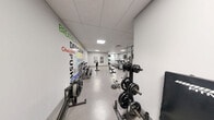 Located at 220 Ira Needles Boulevard in Kitchener, Ontario, this fitness facility offers a comprehensively outfitted exercise room designed to support a wide range of workout routines. The space is finished with a clean, modern aesthetic, featuring light grey walls, a speckled epoxy floor, and a drop-tile ceiling with recessed panel lighting that keeps the environment bright and functional.

The cardio section is well-appointed with multiple treadmills — each paired with wall-mounted flat-screen televisions for entertainment during workouts — as well as elliptical trainers and stationary spin bikes. For strength training, the facility includes a power rack loaded with weight plates, a dumbbell rack stocked with a full range of free weights, a rowing machine, and an adjustable workout bench. Stability and medicine balls round out the functional fitness offerings.

A standout feature of the space is the large motivational mural covering one full wall, displaying bold, colourful typography with words such as "Dedication," "Strength," "Aim Higher," and "Commitment," creating an energizing and inspiring atmosphere. A full-length mirror on the opposing wall supports form-checking during training. The layout is thoughtfully organized to allow comfortable movement between equipment zones, making this a practical and motivating environment for residents seeking a convenient on-site fitness option.