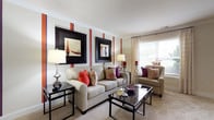 This two-floor residence offers a thoughtfully designed layout with a warm and cohesive aesthetic carried throughout each room. The living room is a standout space, featuring bold burnt-orange vertical accent stripes on the walls, crown molding, and large framed artwork. Neutral carpet, a glass-top coffee table, and plush seating create an inviting and well-balanced atmosphere, complemented by natural light streaming through large windows dressed in patterned drapes. Adjacent to the living area, the dining room continues the warm color palette with a rich terracotta accent wall, wainscoting, and a glass-top dining table surrounded by upholstered chairs. The kitchen is equipped with warm wood cabinetry, white appliances including a range, dishwasher, and refrigerator, tile flooring, and ample counter and storage space, with a deep red backsplash adding a vibrant touch. The primary bedroom features double closets, soft carpeting, and coordinating accent details along the upper walls. A second bedroom provides comfortable proportions with its own closet and carpeted flooring. A carpeted hallway connects the bedrooms and bathrooms efficiently. The bathrooms include white tile flooring and clean, functional finishes throughout.