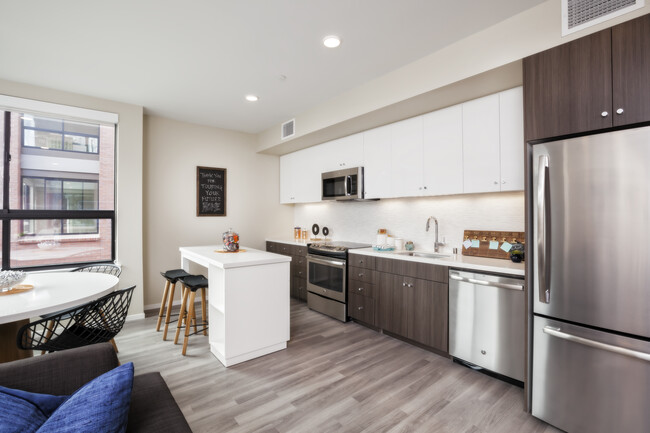 Open concept kitchen with stainless steel appliances, white and brown cabinetry, quartz stone countertop, ceramic tile backsplash, island table and hard surface flooring - Avalon Dogpatch