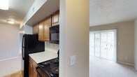 This single-floor residence offers a practical and comfortable layout designed to make the most of its footprint. The kitchen is efficiently organized, featuring warm wood cabinetry with ample upper storage, light-toned countertops, a black electric range, and a built-in over-the-range microwave. The dark appliances contrast neatly against the lighter cabinetry and counters, giving the kitchen a clean, cohesive look. A textured ceiling adds subtle visual depth throughout the space. Adjacent to the kitchen, the living area is carpeted and benefits from an abundance of natural light streaming in through a large sliding glass door. The slider opens to an outdoor area, enhancing the sense of openness and providing a seamless connection between the interior and exterior. The neutral color palette of warm beige tones on the walls and flooring creates a welcoming and versatile atmosphere, making it easy to personalize the space. Overall, the layout flows naturally from the kitchen into the living area, offering a functional and inviting environment well-suited for everyday living.