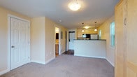 This single-floor residence offers a practical and comfortable layout with a warm, neutral color palette of soft yellow walls and white trim throughout. The open-concept living area features plush wall-to-wall carpeting and flows seamlessly into the kitchen, creating a connected and spacious feel. The kitchen is well-equipped with stainless steel appliances, including an electric range, over-the-range microwave, and refrigerator, complemented by dark granite-style countertops, light wood cabinetry, and richly toned slate tile flooring. A breakfast bar with pendant lighting serves as both a functional workspace and a casual dining area. Conveniently tucked adjacent to the kitchen is an in-unit stacked washer and dryer, adding everyday practicality. The bedroom is generously sized, filled with natural light from multiple windows that offer views of surrounding greenery, and features a large built-in wood wardrobe unit providing substantial storage. The bathroom is clean and efficiently designed, with tile flooring, a pedestal sink, a wall-mounted mirror with vanity lighting, and overhead cabinetry for additional storage. Overall, the space presents a cohesive, functional, and move-in-ready environment.