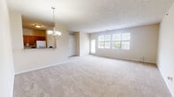 This single-floor residence offers a practical and comfortable layout comprising two bedrooms, two bathrooms, a kitchen, a hallway, and two closets. The open living and dining area is a standout feature, finished with neutral-toned carpet and anchored by an elegant chandelier that adds a refined touch. Large windows along the exterior wall flood the space with natural light and provide views of the surrounding greenery. A textured ceiling adds subtle architectural character to the living area.

The kitchen is equipped with warm honey-toned wood cabinetry, ample counter space with dark laminate countertops, a white range with overhead ventilation, and tile flooring — offering a functional and organized cooking environment. A pass-through counter connects the kitchen to the living and dining area.

The primary bedroom is generously sized and features plush carpeting, a large window for natural light, and access to a spacious walk-in closet outfitted with wire shelving and hanging rods for ample storage. The second bedroom is similarly carpeted and well-proportioned, with its own closet. Both bathrooms are cleanly finished, with one featuring a single-sink vanity with wood cabinetry and a tub-shower combination. Throughout the residence, neutral wall tones and consistent flooring create a cohesive and welcoming ambiance.