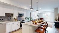 Located in the heart of Denver, CO, this thoughtfully designed one-bedroom, one-bathroom residence offers a seamless blend of modern style and urban convenience. The open-concept kitchen and living area serves as the centerpiece of the home, featuring white shaker cabinetry, stainless steel appliances, a subway tile backsplash, and a large island with bar seating illuminated by striking geometric pendant lights. Wood-style flooring flows throughout, adding warmth to the contemporary palette. The living room is bathed in natural light from oversized windows that frame expansive city views, with direct access to a private balcony overlooking the Denver skyline. The bedroom offers a serene retreat, highlighted by a textured accent wall, plush carpeting, a ceiling fan, and a large window with additional city views. A dedicated closet provides generous storage. The bathroom is finished with a wide floating vanity, an undermount sink, matte black fixtures, and a backlit mirror that lends a spa-like ambiance. Clean lines and neutral tones create a cohesive, modern aesthetic throughout the entire residence, making it an ideal home for those seeking stylish urban living in Denver's vibrant civic center neighborhood.