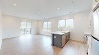 This single-floor space showcases a clean, contemporary design highlighted by a bright, open-concept layout. The kitchen serves as the centerpiece, featuring a large island with a slate-blue base, white quartz countertops, an integrated sink, and stainless steel appliances including a refrigerator, range, and microwave. White shaker-style upper cabinetry provides ample storage, while light hardwood-style flooring extends seamlessly into the adjacent living area. Recessed lighting throughout ensures consistent, well-distributed illumination. Large windows flood the living space with natural light and offer elevated views of the surrounding neighborhood and greenery. A sliding door leads to a private balcony, extending the living space outdoors. The bedrooms are finished with plush neutral carpeting and feature windows with outdoor views, creating comfortable, well-lit retreats. A dedicated storage alcove with recessed lighting adds practical utility. Both bathrooms are outfitted with white cabinetry, quartz vanity tops, tub-shower combinations, and brushed gold hardware accents, contributing a refined touch. The overall aesthetic is modern, clean, and move-in ready.