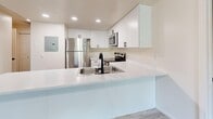 Located at 7875 S Candlestick Ln in Midvale, Utah, this well-appointed single-floor home offers three bedrooms, two bathrooms, and a thoughtfully designed layout. The open-concept kitchen is a standout feature, showcasing crisp white cabinetry, stainless steel appliances including a refrigerator, range, microwave, and dishwasher, and a peninsula with a white countertop and undermount sink with a matte black faucet. Light wood-style vinyl flooring ties the kitchen and adjacent spaces together seamlessly. The spacious living room is bright and inviting, featuring a fireplace flanked by multiple windows that allow natural light to fill the room. The primary bedroom is highlighted by a distinctive arched window that frames outdoor greenery, complemented by soft carpet flooring. The additional bedrooms are carpeted and receive natural light through standard windows. Both bathrooms are finished consistently with wood-style vinyl flooring, white vanity cabinetry, and a tub/shower combo with matte black fixtures. A dedicated closet provides additional storage. The home's neutral color palette, clean finishes, and cohesive design create a comfortable, move-in-ready environment throughout.