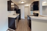 This three-floor home is designed with a functional and straightforward layout across its levels. The main living area features wood-look plank flooring in a neutral grey tone, complemented by warm beige walls and white trim throughout. A pass-through kitchen connects to the living space, outfitted with dark espresso cabinetry, light countertops, stainless steel appliances including a refrigerator and dishwasher, and a built-in sink. A large window in the living area allows natural light to fill the space, which also features staircase access to upper levels.

The upper floor hosts carpeted bedrooms finished in warm beige tones. Each bedroom includes a window with vertical blinds for natural light and privacy, and at least one room features a dedicated walk-in closet with built-in shelving. The bathrooms are well-appointed, with one featuring warm wood-tone cabinetry, a single vanity with a large mirror, and a tub, while another includes a stand-up shower with a frosted glass door and an overhead storage cabinet.

The unfinished basement level offers a generously sized open space with painted concrete floors, white walls, and exposed ceiling joists, housing the home's HVAC utility systems.