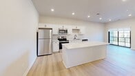 Located at 8484 Brougham Dr. in Sterling Heights, MI, this thoughtfully designed one-bedroom, one-bathroom unit offers a clean, modern aesthetic across a single floor. Light-toned hardwood-style flooring flows throughout, complementing the bright, neutral color palette that gives the space an open and airy feel.

The kitchen is a standout feature, equipped with stainless steel appliances including a refrigerator, range, microwave, and dishwasher. Crisp white cabinetry, a classic subway tile backsplash, and a large white center island provide ample storage and prep space, making it both functional and visually appealing. Recessed lighting illuminates the area effectively.

The bedroom is a comfortable, well-proportioned retreat featuring light wood-style flooring, neutral walls, and a window fitted with blinds that overlook a lush, tree-lined exterior — allowing for natural light while maintaining privacy. A dedicated closet adds practical storage.

The bathroom features a walk-in shower enclosed by sleek black-framed sliding glass doors, with built-in shelving niches and white tile surroundings, accented by matte black hardware for a contemporary touch. The unit is rounded out by a utility room, completing a well-organized and efficiently laid-out living space.