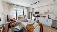 Located at 2501 38th Ave NE in St. Anthony, Minnesota, this single-floor unit offers a thoughtfully designed open-concept layout that seamlessly connects the living, dining, and kitchen areas. Large floor-to-ceiling windows flood the living space with natural light and provide views of the surrounding neighborhood, creating an airy, welcoming atmosphere. Track lighting overhead adds a modern, functional touch throughout.

The kitchen is well-appointed with white cabinetry featuring black hardware, a subway tile backsplash, stainless steel appliances including a refrigerator, electric range, microwave, and dishwasher, along with ample counter and storage space. Light wood-tone flooring runs consistently throughout the unit, enhancing the cohesive, contemporary aesthetic.

The bedroom is a calm retreat with a ceiling fan, a spacious sliding-door closet, and soft neutral tones. The bathroom is clean and modern, featuring white walls, light wood flooring, a full soaking tub with a shower, matte black fixtures, and a floating vanity with generous storage. Overall, the unit presents a sleek, functional design with a warm and inviting ambiance.