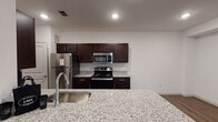 This well-appointed single-floor unit offers a thoughtfully designed open layout that seamlessly connects the main living areas. The kitchen serves as a focal point, showcasing a large granite island with an undermount sink, rich dark-espresso cabinetry, granite countertops, and a full suite of stainless steel appliances including a refrigerator, range, and over-the-range microwave. Recessed lighting illuminates the space, which flows directly into the open living area featuring warm wood-look plank flooring throughout. The living room is generously sized, bathed in natural light from dual windows that frame views of surrounding greenery, and features vaulted ceiling details that enhance the sense of openness. Arched architectural accents add a classic touch to the interior transitions. The bedrooms are finished with plush carpet and include windows with blinds for natural light and privacy. The bathrooms are consistent in their design, featuring granite vanity tops, dark-framed mirrors, and chrome fixtures; one includes a soaking tub with shower combination. A dedicated in-unit laundry room with a washer and dryer provides added everyday convenience, completing this practical and attractive living space.