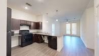 This well-appointed single-story home in Austin, TX offers four bedrooms and two bathrooms across a thoughtfully designed floor plan. The open-concept kitchen and living area serves as the heart of the home, featuring rich dark espresso cabinetry, granite countertops, a peninsula island with pendant lighting overhead, and black appliances including a gas range and dishwasher. Light wood-look flooring flows throughout the main living areas, while a ceiling fan and large windows with blinds allow natural light to fill the space and offer views of the surrounding neighborhood.

The bedrooms are carpeted for comfort and include windows that bring in natural light. The primary bedroom features a walk-in closet with built-in wire shelving. The bathrooms are designed with accessibility in mind, showcasing ADA-compliant features such as grab bars, open under-sink vanities, and roll-in shower accessibility. Dark wood cabinetry and large mirrors complement the clean white countertops in both bathrooms. A hallway connects the bedrooms and living spaces, contributing to an efficient and practical layout. The home's neutral color palette and clean finishes create a bright, move-in-ready atmosphere throughout.