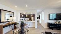The 1660 Metro #202 Model in Chula Vista presents a thoughtfully designed single-floor residence with a contemporary aesthetic throughout. The open-concept living, dining, and kitchen area forms the heart of the home, where light wood-style flooring flows seamlessly underfoot. The kitchen is outfitted with dark espresso cabinetry, white quartz countertops, stainless steel appliances, and pendant lighting, with a peninsula that connects to the dining space. The living room features a striking sputnik-style chandelier, a large window allowing natural light, and ample room for comfortable seating arrangements.

Two well-proportioned bedrooms each feature plush carpeting, generous windows with blinds, and clean white walls. The primary bedroom includes access to a walk-in closet and an adjoining bathroom. Both bathrooms mirror the kitchen's design language, featuring dark espresso vanities, white countertops, large mirrors, wood-style tile flooring, and combination tub-shower units. The overall palette of white walls, dark cabinetry, and warm flooring creates a cohesive, modern ambiance that balances style with functionality throughout the residence.