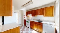 Located at 3201 Lancaster Avenue in Wilmington, Delaware, this single-floor residence offers a practical and comfortable layout across two bedrooms, one bathroom, and a dedicated kitchen, connected by two hallways. The kitchen is a standout feature, outfitted with warm honey-toned wood cabinetry extending to the upper walls, ample counter space, a white electric range, dishwasher, refrigerator, and a stainless steel sink. A classic pink-and-white checkered tile floor adds a distinctive character to the kitchen and bathroom areas. The primary bedroom is generously sized, featuring soft wall-to-wall carpeting, crisp white walls, and multiple windows — including a corner bay-style window — that invite abundant natural light. The second bedroom mirrors this brightness with carpeted flooring and window access to natural light. The bathroom is cleanly appointed with a wood-vanity cabinet, wall mirror, a window for ventilation and light, and a full bathtub with shower. Hallways connect the rooms efficiently, contributing to a straightforward and functional floor plan. The neutral color palette throughout creates a clean, move-in-ready atmosphere well-suited for comfortable everyday living.