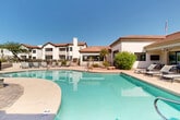 Located at 4221 E Ray Rd in Phoenix, Arizona, this outdoor amenity space showcases a beautifully designed resort-style pool area that embodies the essence of Southwestern living. The centerpiece is a generously sized, freeform swimming pool with crystal-clear turquoise water, complemented by a separate spa with a raised surround that invites relaxation under the Arizona sun.

The pool deck is finished in a warm, textured concrete surface and is lined with a generous arrangement of lounge chairs, providing ample space for sunbathing. A standout feature of the space is a covered gazebo equipped with elegant teal curtains, outdoor dining furniture, and a built-in grill — ideal for al fresco entertaining. An additional covered patio area adjacent to the clubhouse structure offers shaded seating and dining options.

The surrounding architecture features white stucco exteriors with distinctive terracotta tile rooflines, characteristic of classic Arizona design. Desert-adapted landscaping, including palm trees, ornamental grasses, and native shrubs, frames the space naturally. The open sky above ensures abundant natural light throughout the day, while the fenced perimeter provides privacy and security. This thoughtfully appointed outdoor space offers a complete and inviting recreation experience.